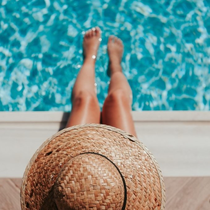 woman sitting on poolside setting both of her feet on pool